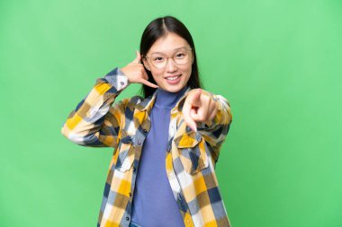 Young Asian woman over isolated chroma key background making phone gesture and pointing front