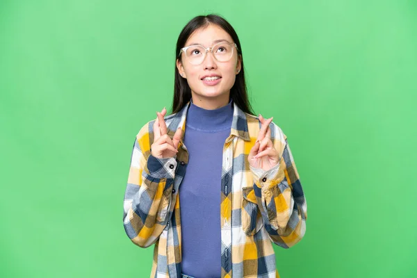 Young Asian woman over isolated chroma key background with fingers crossing and wishing the best