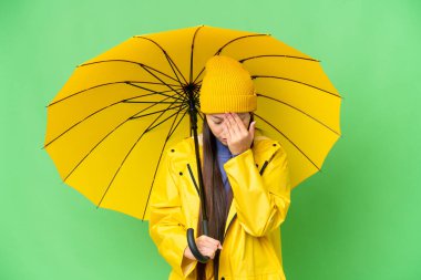 Young Asian woman with rainproof coat and umbrella over isolated chroma key background with tired and sick expression