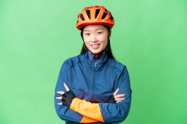 Young cyclist woman over isolated chroma key background keeping the arms crossed in frontal position