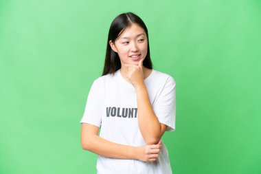 Young volunteer woman over isolated chroma key background looking to the side and smiling