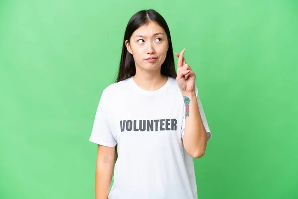 Young volunteer woman over isolated chroma key background with fingers crossing and wishing the best