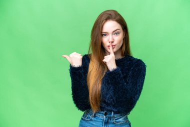 Young pretty woman over isolated chroma key background pointing to the side and doing silence gesture