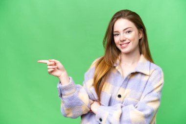 Young pretty woman over isolated chroma key background pointing finger to the side