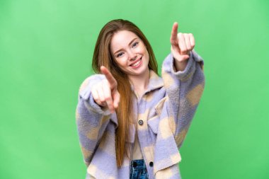 Genç ve güzel bir kadın izole edilmiş krom anahtar arka planda mutlu bir ifadeyle ön tarafı işaret ediyor.