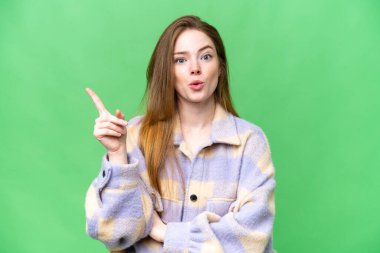 Genç ve güzel bir kadın izole edilmiş krom anahtar arka planda bir parmağını kaldırarak çözümü anlamaya çalışıyor.