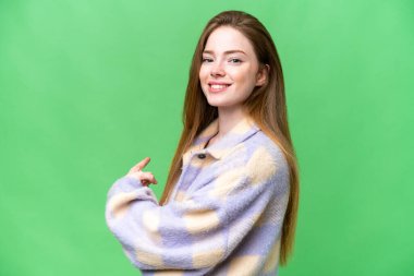 Young pretty woman over isolated chroma key background pointing back