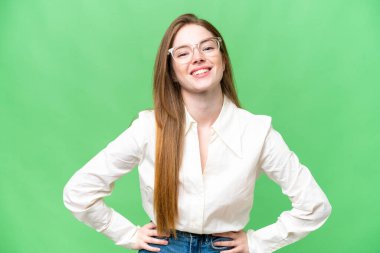 Young pretty woman over isolated chroma key background posing with arms at hip and smiling