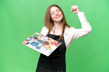 Young artist woman holding a palette over isolated chroma key background celebrating a victory