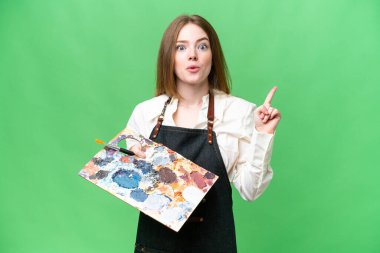 İzole edilmiş krom anahtar arkaplan üzerinde palet tutan genç sanatçı kadın çözümü fark etmek için bir parmağını kaldırarak