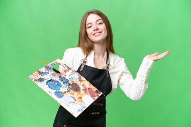 İzole edilmiş krom arka planda palet tutan genç bir sanatçı. Gelmesi için ellerini yana uzatıyor.