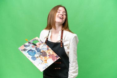 Young artist woman holding a palette over isolated chroma key background laughing