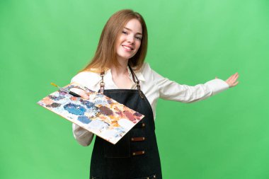 İzole edilmiş krom arka planda palet tutan genç bir sanatçı. Gelmesi için ellerini yana uzatıyor.