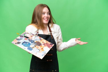 Young artist woman holding a palette over isolated chroma key background with surprise expression while looking side