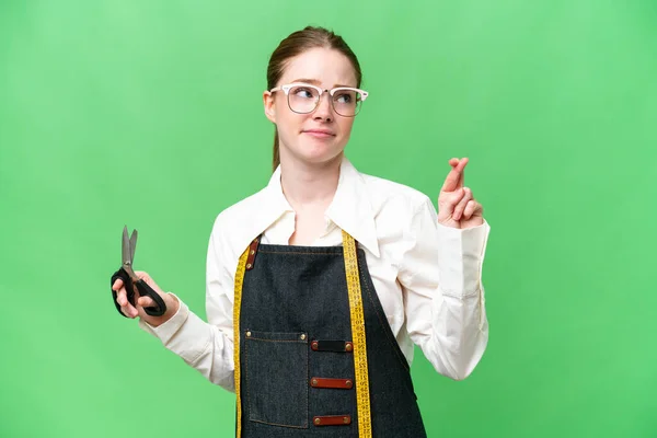 Seamstress woman over isolated chroma key background with fingers crossing and wishing the best