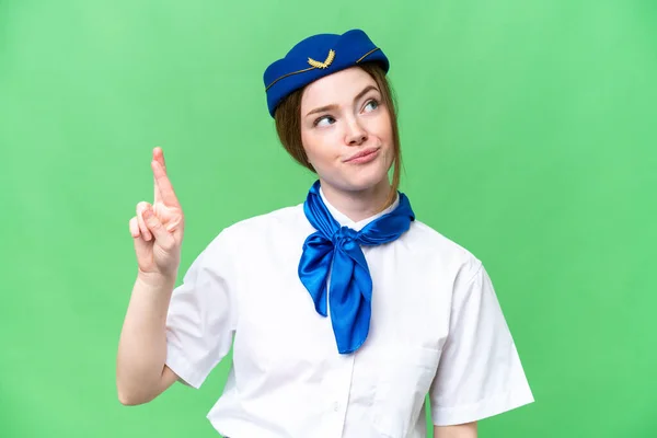 Airplane stewardess over isolated chroma key background with fingers crossing and wishing the best