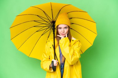 Young pretty woman with rainproof coat and umbrella over isolated chroma key background thinking