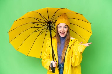 Young pretty woman with rainproof coat and umbrella over isolated chroma key background with shocked facial expression