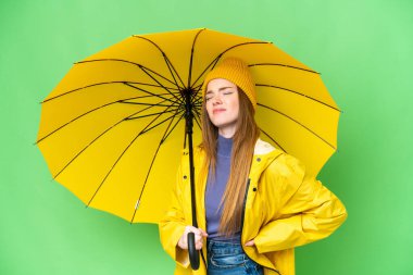 Young pretty woman with rainproof coat and umbrella over isolated chroma key background suffering from backache for having made an effort
