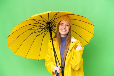 Young pretty woman with rainproof coat and umbrella over isolated chroma key background making money gesture