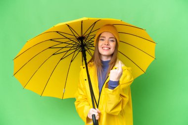 Young pretty woman with rainproof coat and umbrella over isolated chroma key background doing coming gesture