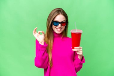 Young woman holding soda while watching a 3D movie showing ok sign with fingers