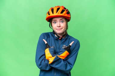 Young cyclist woman over isolated chroma key background pointing to the laterals having doubts