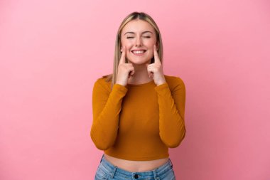 Pembe arka planda izole edilmiş genç beyaz kadın mutlu ve hoş bir ifadeyle gülümsüyor.