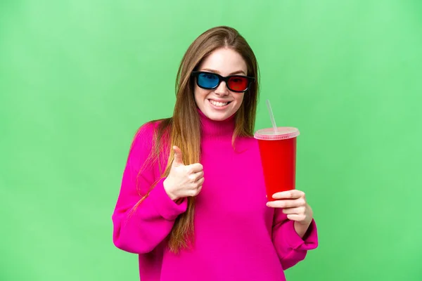 Young woman holding soda while watching a 3D movie with thumbs up because something good has happened