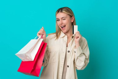 Mavi arka planda izole edilmiş beyaz bir kadın elinde alışveriş çantaları ve bir kredi kartı tutuyor.