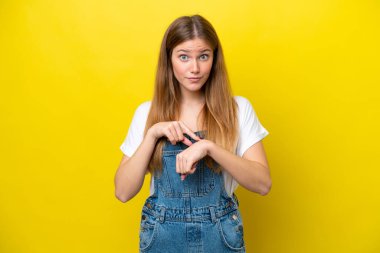 Sarı arka planda izole genç beyaz kadın geç kalma jesti yapıyor.