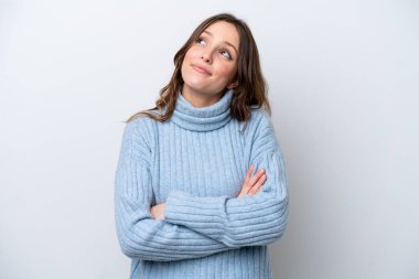 Beyaz arka planda izole edilmiş genç beyaz kadın gülümserken yukarı bakıyor.