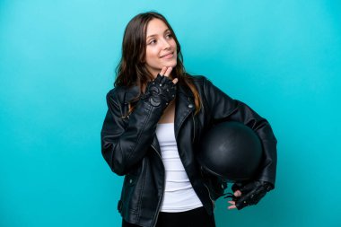 Mavi arka planda izole edilmiş motosiklet kasklı beyaz bir kadın gülümserken yukarı bakıyor.