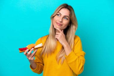 Young Uruguayan woman holding sashimi isolated on blue background looking up while smiling