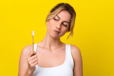 Young Uruguayan woman brushing teeth isolated on yellow background with sad expression