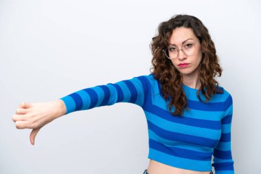 Beyaz arka planda izole edilmiş genç beyaz kadın olumsuz ifade ile baş parmağını aşağı gösteriyor.