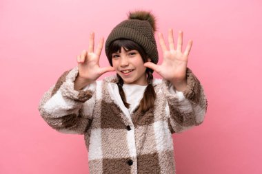 Little caucasian girl with winter jacket isolated on pink background counting eight with fingers