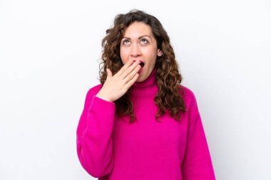 Beyaz arka planda izole edilmiş genç beyaz bir kadın esniyor ve geniş bir ağzı eliyle kapatıyor.