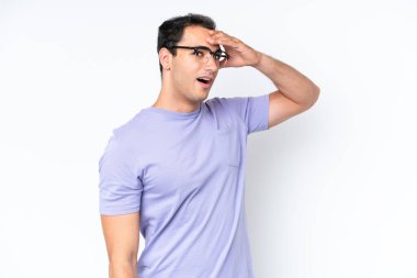 Beyaz arka planda izole edilmiş genç beyaz adam yan tarafa bakarken sürpriz jest yapıyor.