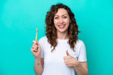 Mavi arka planda dişlerini fırçalayan beyaz bir kadın. Başparmakları havada. Çünkü iyi bir şey oldu.