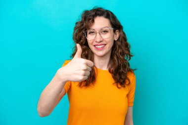 Mavi arka planda, gözlüklü ve baş parmağıyla izole edilmiş beyaz bir kadın.