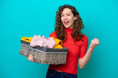 Young caucasian woman holding a clothes basket isolated on blue background celebrating a victory