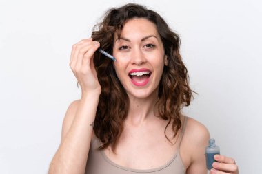 Beyaz arka planda izole edilmiş beyaz bir kadın elinde bir serum tutarken gülümsüyor. Portreyi kapat