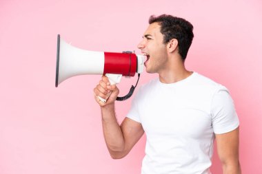 Pembe arka planda izole edilmiş genç beyaz bir adam megafondan bir şey duyurmak için bağırıyor.