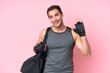 Young sport caucasian man with sport bag isolated on pink background saluting with hand with happy expression