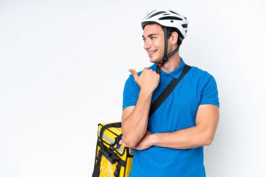 Beyaz arka planda izole edilmiş termal sırt çantalı beyaz bir adam bir ürün sunmak için kenarı işaret ediyor.