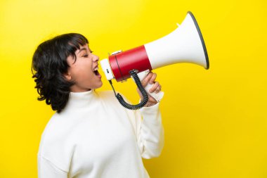 Arjantinli genç bir kadın sarı arka planda izole edilmiş bir şekilde megafondan bağırıyor.