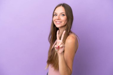 Mor arka planda izole edilmiş genç Litvanyalı kadın gülümsüyor ve zafer işareti gösteriyor.