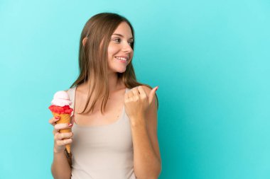 Young Lithuanian woman with cornet ice cream isolated on blue background pointing to the side to present a product