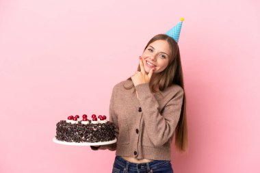 Young Lithuanian woman holding birthday cake isolated on pink background happy and smiling